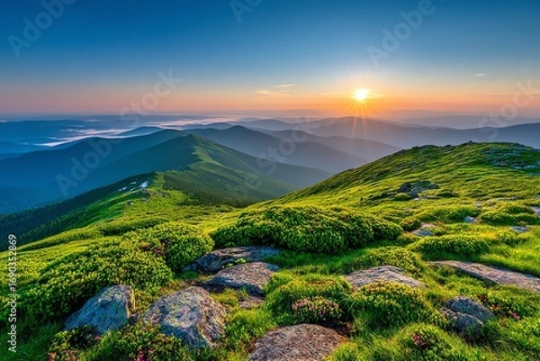Fototapeta A vibrant sunset illuminates a rolling mountain landscape, showcasing lush green meadows dotted with wildflowers and rocky outcrops, evoking a sense of peaceful serenity and natural beauty.