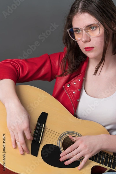 Fototapeta Portrait of female guitarist, she holding her musical instrument in front of her, with guitar resting on lap. She looking intently into distance, suggesting state of deep contemplation, concentration