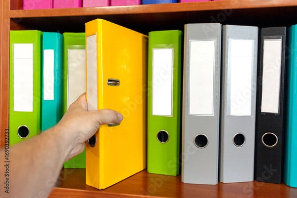 Fototapeta A man takes a folder with documents from a shelf.