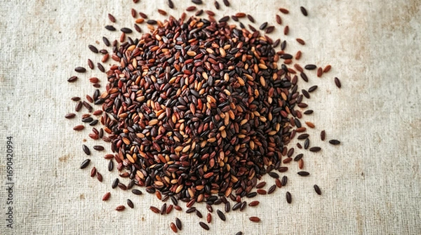 Fototapeta A pile of black rice, also known as forbidden rice, scattered on a textured burlap surface. The grains have a deep, dark hue with some reddish-brown undertones.