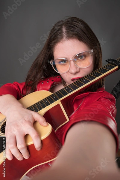 Fototapeta Female guitarist and vlogger for hype bites her guitar's neck and takes selfie during performance. This is an example of user generated content