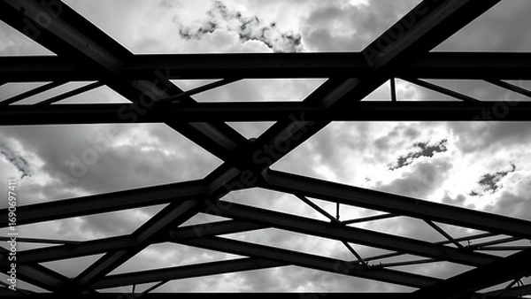 Fototapeta Steel beams forming geometric patterns against a cloudy sky, emphasizing industrial design.