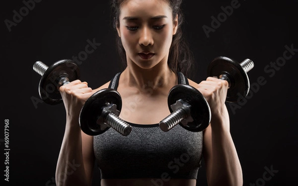 Obraz Beautiful girl exercising squatting with dumbbells on black.