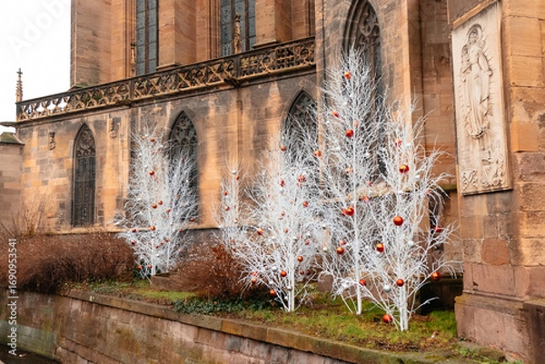 Fototapeta Frosted white trees adorned with red ornaments create a festive atmosphere around the historic church, inviting visitors to enjoy the holiday spirit in this lively city.