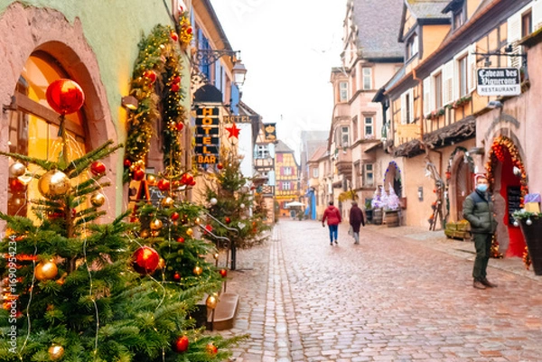 Fototapeta Colorful decorations and Christmas trees line the cobblestone streets as visitors explore the holiday market, enjoying the seasonal atmosphere on a cool day.