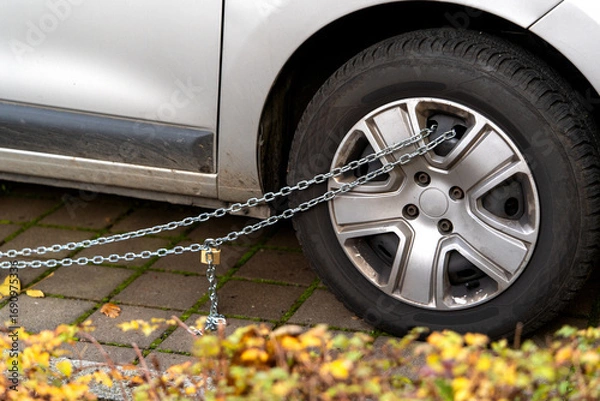 Fototapeta Car wheel locking with metal chain and padlock, preventing movement. Theft protection or as penalty for illegal parking. Personal vehicle security. DIY safety methods for property protection