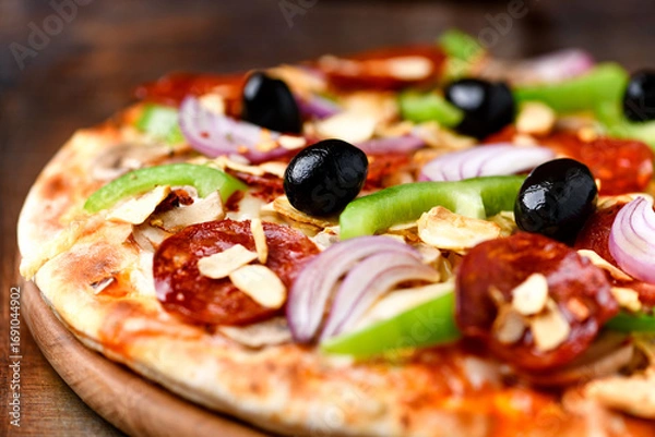 Fototapeta Pizza with chorizo ​​sausage, mozzarella cheese, green pepper and black olives. Rustic wooden background. Soft focus.