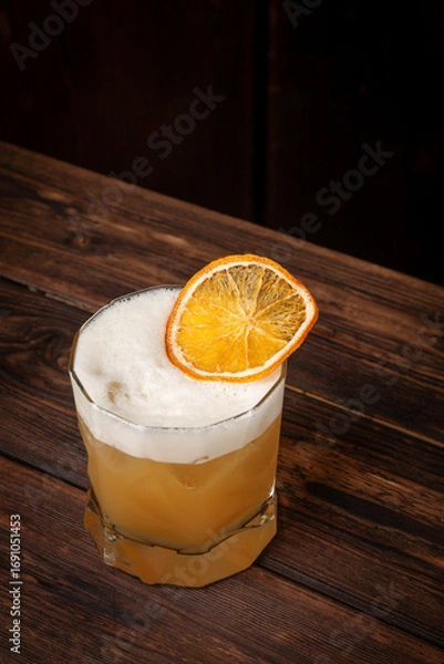 Fototapeta Citrus yellow cocktail with airy foam and dried orange garnish served in short glass on rustic wooden table