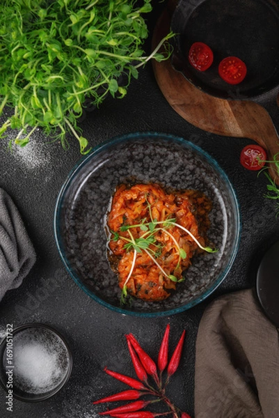 Fototapeta Traditional stewed cabbage in tomato sauce with fresh herbs served in dark ceramic bowl on rustic table