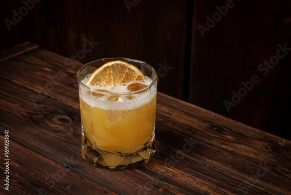 Fototapeta Classic whiskey sour cocktail with ice cubes and dried orange slice served in lowball glass on rustic wooden table