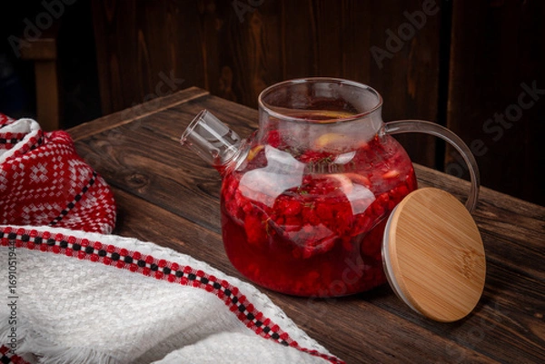 Fototapeta Hot berry fruit tea with fresh raspberry, lemon slices and herbs served in transparent glass teapot on rustic wooden table