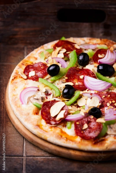 Fototapeta Pizza with chorizo ​​sausage, mozzarella cheese, green pepper and black olives. Rustic wooden background. Soft focus.