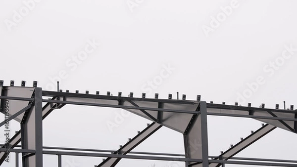 Fototapeta Metal construction, in the photo the structure of the building frame made of metal beams against the background of a gray sky