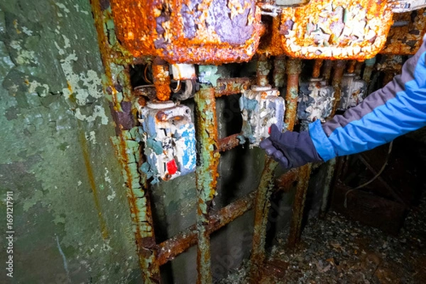 Fototapeta Pressing a button by hand on control panel in an old abandoned bunker with peeling paint and damp walls.