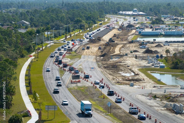 Fototapeta Highway construction in North Port, Florida. Development of American road with moving traffic cars. City transportation improvement