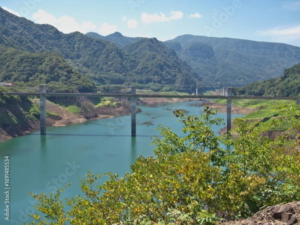 Fototapeta Gunma, Japan - September 7, 2025: Appeared due to drought, submerged disused railroad tracks, roads, basements and trees under the water of Yamba Dam in Gunma, Japan