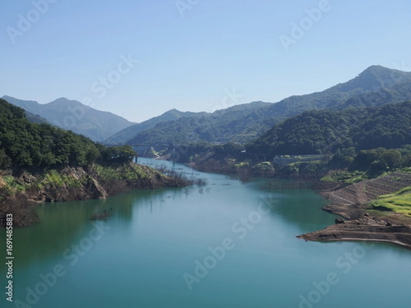 Fototapeta Gunma, Japan - September 7, 2025: Appeared due to drought, submerged disused railroad tracks, roads, basements and trees under the water of Yamba Dam in Gunma, Japan