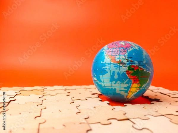 Fototapeta The image shows a colorful globe, which is a puzzle, resting on a surface covered with scattered, unassembled puzzle pieces