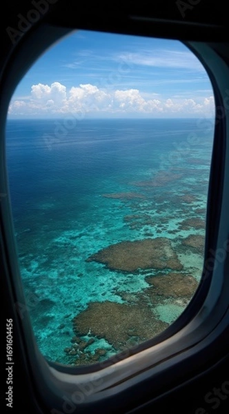 Fototapeta Airplane window view of turquoise ocean waters meeting land under a partly cloudy blue sky during a daytime flight, emphasizing travel and exploration
