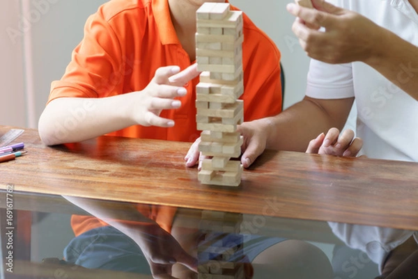 Fototapeta Asian father and son playing wood blocks game Carefree kid playing wood blocks game building constructor from blocks with father at home