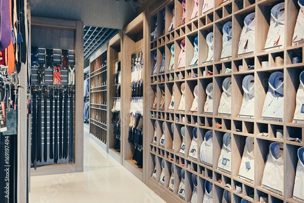 Obraz wnętrze butiku do sprzedaży garniturów biznesowych. Na półkach duży wybór kolorowych koszul