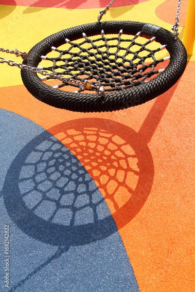 Fototapeta A black spider web swing in colorful playground. Resemble bird nest in shape and able to carry multiple people. One of popular play installation at children's playground.