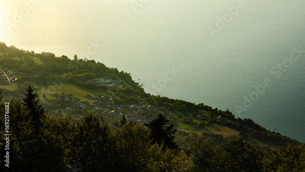 Obraz Vue plongeante depuis les sommet sur la ville et la lac d'Évian-les-Bains au lever du jour quand les premiers rayons du soleil colorent l'eau d'or et de turquoise.