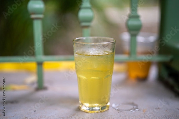 Fototapeta Refreshing yellow drink in a glass with ice on a summer day.