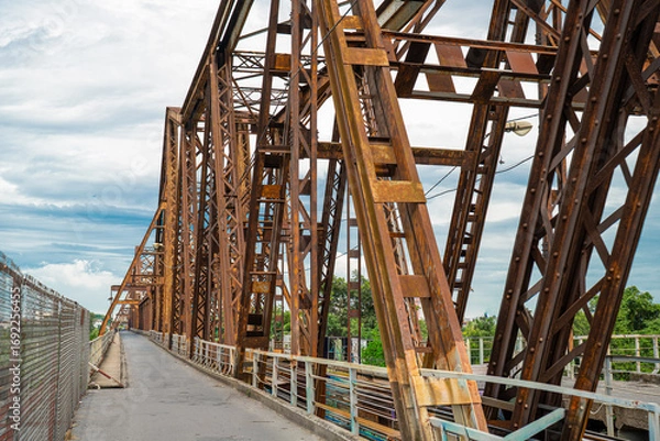 Fototapeta Rusty steel bridge with a scenic backdrop on a cloudy day.
