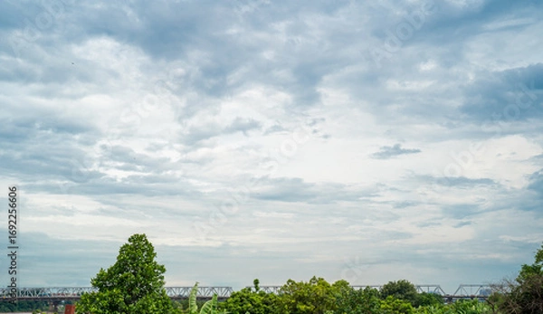 Fototapeta A serene landscape featuring a cloudy sky and lush green trees.