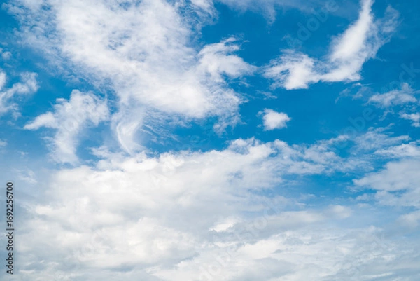 Fototapeta A vibrant blue sky with fluffy white clouds illuminated by soft sunlight.