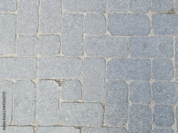 Fototapeta Gray cobblestone pavement texture. Top view of a timeless stone block path or road, a perfect rustic and durable background for design and architectural projects.