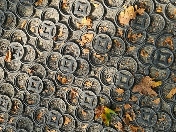 Fototapeta Abstract autumn background with dry leaves on a patterned rubber grid pavement. The circular, geometric texture of the ground contrasts with the organic shapes of the fall foliage.