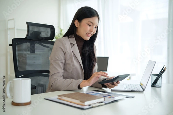 Fototapeta Asian businesswoman using a calculator while working at her desk.