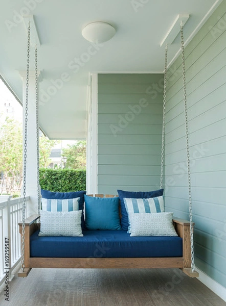 Fototapeta outdoor wooden porch swing bench with blue pillows.