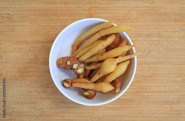 Fototapeta Finger root or Chinese ginger in white bowl on bamboo wooden background, preparation process for cooking. Top view.
