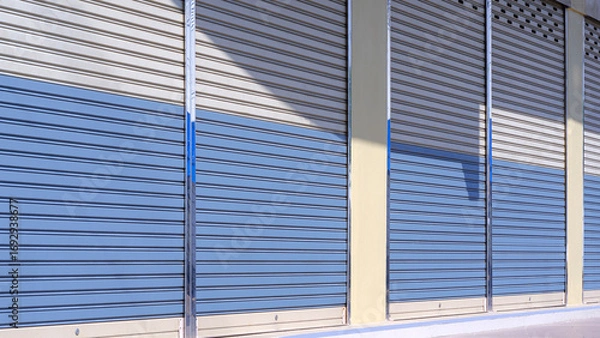 Fototapeta Automatic roller shutter doors of commercial building background with light and shadow on surface, side view with copy space