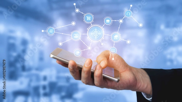 Fototapeta A hand holding a smartphone is displayed against a blue background, showcasing digital network icons symbolizing modern communication and technology integration in business. Tessel