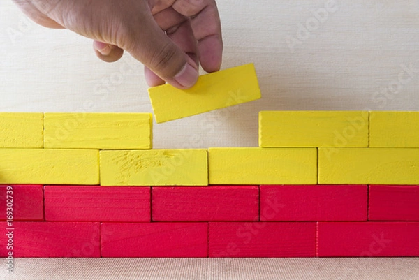 Fototapeta Two fingers put the last red block on the wall, Metaphoric scene,Building concept