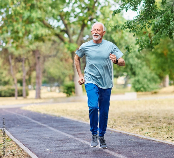 Fototapeta Smiling active mature elderly man jogging running in the park