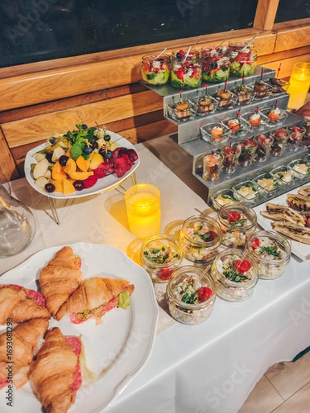 Obraz A diverse buffet spread on a yacht boat deck, ready for guests. Catering buffet for events. Catering banquet table with different food snacks and appetizers with sandwich, salads, fresh fruits. 