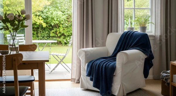 Obraz Cozy armchair with a blue blanket in a bright living room overlooking a garden creating a peaceful and inviting atmosphere for relaxation