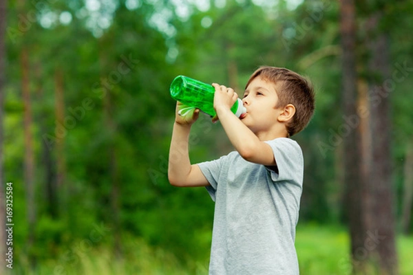 Fototapeta Little boy drinking water from a bottle after playing sports. Child resting after running.