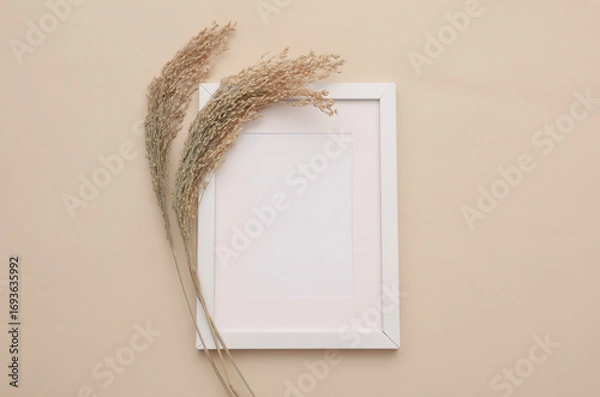 Fototapeta Mockup of white photo frame with dry grass on beige background