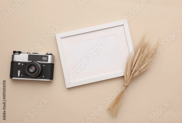 Fototapeta Mockup of white photo frame with dry grass and film camera on beige background