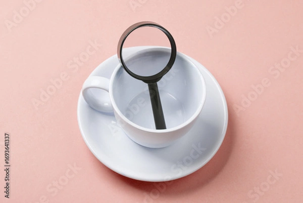 Fototapeta Ceramic cup with a magnifying glass on a pink background