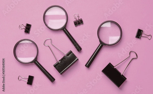 Fototapeta Magnifiers and paper binders on pink background. Top view