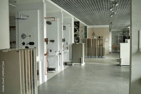 Fototapeta Modern showroom displaying various bathroom fixtures and shower installations with multiple tile samples arranged in foreground, no people visible, spacious commercial interior