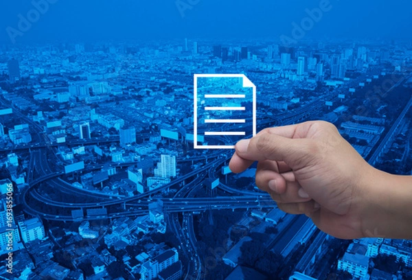 Fototapeta Hand holding document flat icon in fingers over modern city tower, street, expressway and skyscraper, Technology internet online concept