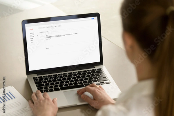Obraz Kobieta pisze e-mail na laptopie przy biurku, pisze profesjonalny list e-mail z zachowaniem etykiety biznesowej, pisze wiadomość e-mail do klienta korporacyjnego online, skupia się na ekranie, zamyka widok z tyłu